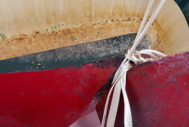 close up of a red, dark green and off-white striped hull of a sailboat.  A knotted white rope is in the photo too. 