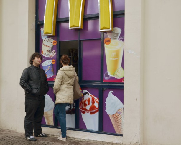 Two people waiting for their order at a McDonalds with a walk up window where you can buy your food without having to go inside.  