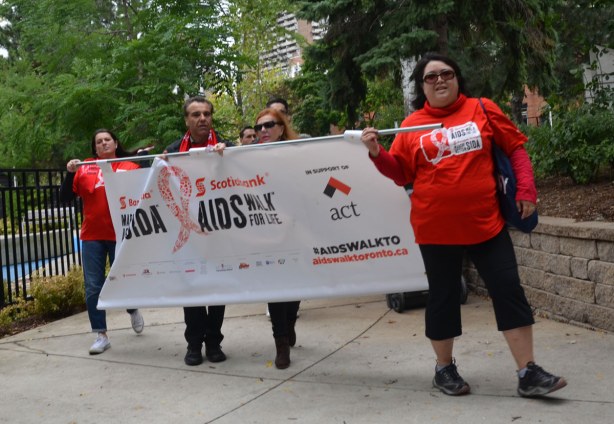 A small group of people is holding a banner in the walk.  The banner says Scotiabank AIDS Walk, in support of ACT .  A C T is AIDS committee Toronto. 
