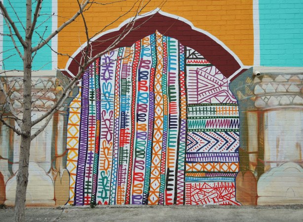 part of a mural, one of four panels painted to look like a yellow and red arch.  under the arch is a bright multicoloured pattern reminiscent of South Asian fabrics and embroidery