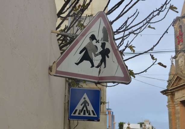 Crossing sign, triangular with red border, of two people holding hands 