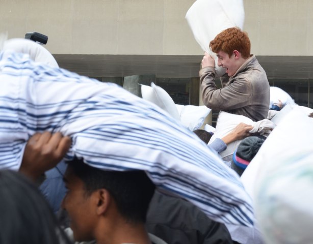 A young red headed man is on the shoulders of another person in a pillow fight. 