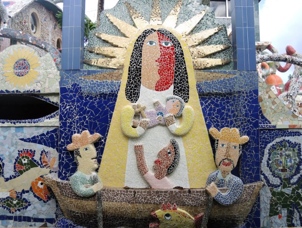 mosaic of a god like figure with gold rays coming from his head.  He is holding a child in his arms.  In front of him is a boat with three men in it. 