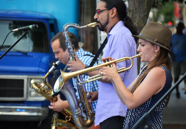 Three brass players performing outside.  Two men on saxophones and a woman playing a trumpet