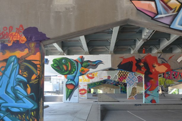 photograph of a number of pillars and supports holding up Eastern Ave as it passes over Lower River St.  Pillars have been painted by street artists including a fish by birdo and lips by Enjoy Denial.   Underpass park.  Toronto