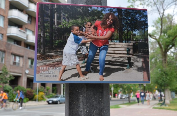 A poster on a lamp pole, a picture of a woman and two boys playing with a ball (pretending to fight over it) 