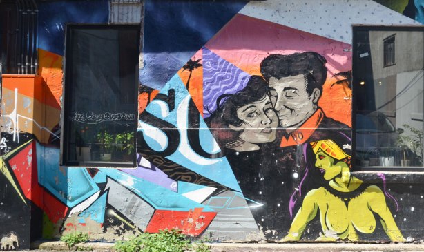 part of a mural on a wall, a couple cheek to cheek with the woman wearing a purple party hat, also a topless green woman