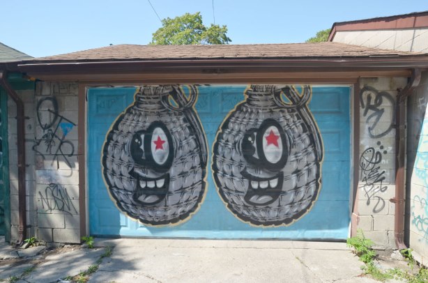 Two spud bomb graffiti characters on a blue garage door in an alley 