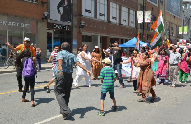 people dancing in a small circle in the middle of Yonge street. They are part of a parade celebrating India's 69th year of independence from Britain. The parade has stopped for a few minutes which has given them time to dance instead of walk. 