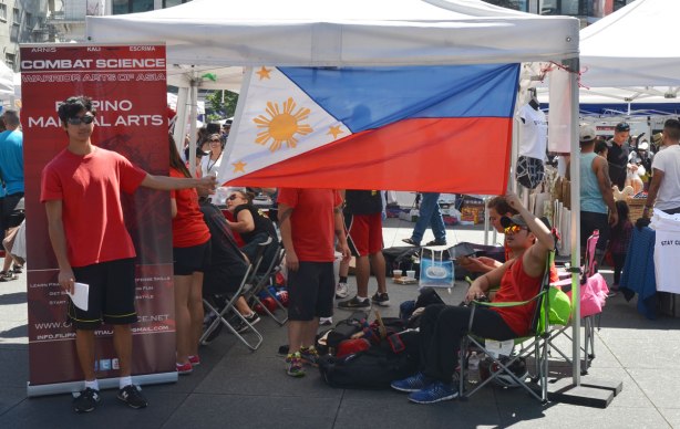 Phillipines flag hanging from the top of an open sided tent. A young man is holding down one of the corners so it doesn't blow in the breeze