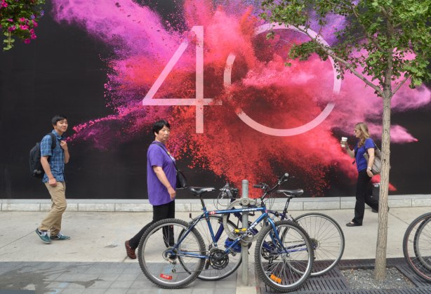 Three people walking past a bright poster for TIFF's 40th year. A burst of pink and orange colour around the number 40, all on a black background. 