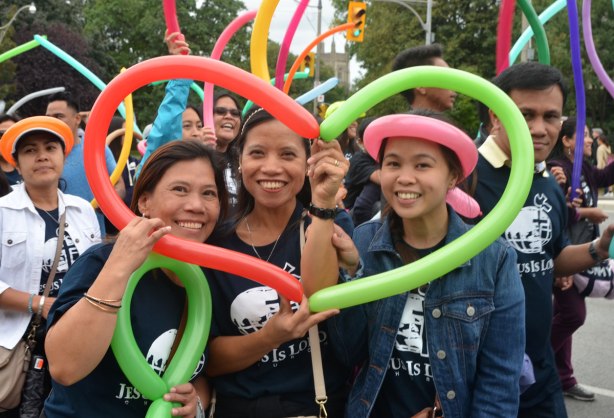 Three young women pose with a heart that they have made out of two long skinny balloons. 