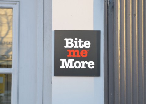 A sign on the wall outside a store that says Bite Me More