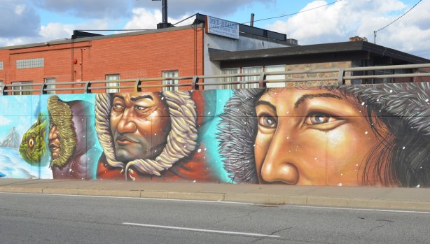 part of a street art mural, three people bundled up in fur lined parkas in a winter scene