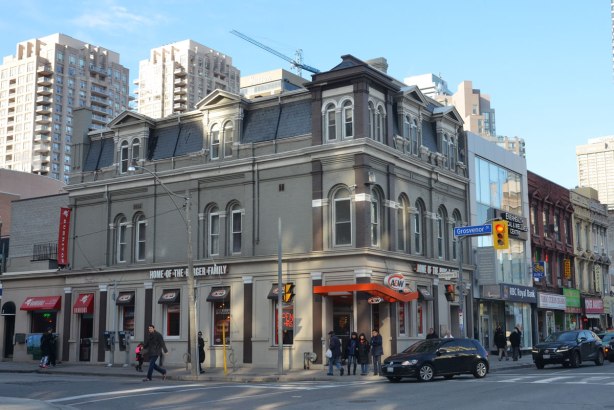 Three storey older grey building on a downtown corner. 
