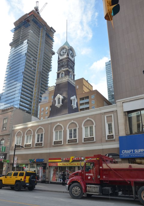 old fire hall tower above a newer building, or a newwer facade on an older building, red dump trunk on the street, large new condo being built in the background, Yonge St. 