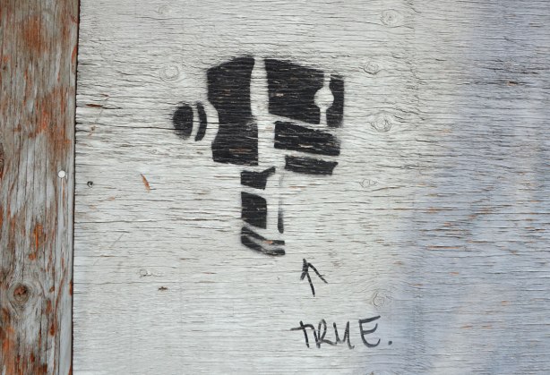 black stencil of an old fashioned video camera. Someone has written the word true under it. 
