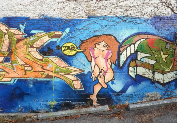 street art on a wall in a laneway. Blue background, naked woman with long brown hair, standing between two tags
