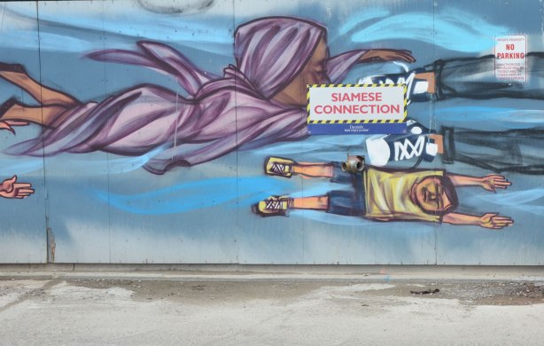 part of a mural of flying people by elicser, a woman in a light purple dress and head scarf as well s a boy in beige Tshirt and blue shorts