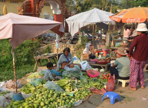 A group of people, women and children, selling vegetables beside the road. 