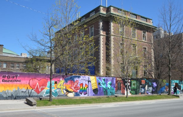 part of a mural on an artwall on hoardings around a construction site for a new engineering building at the University of Toronto, older building behind, long stretch of the mural in the picture