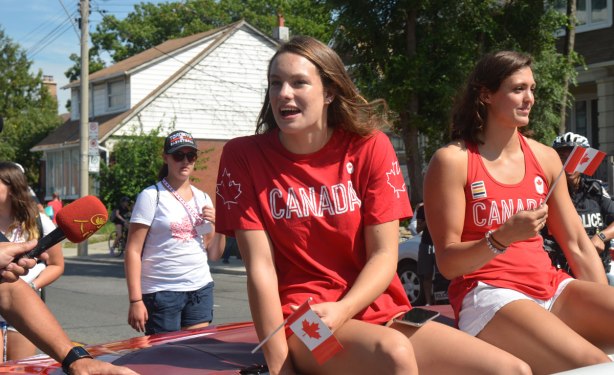 Penny Olesiak and Michelle WIlliams riding in the back of a red convertible in a parade 