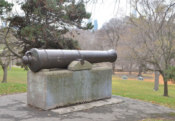 An old cannon from the 1800's stands in a park surround by trees on a grey November day. 