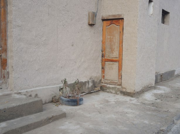 old wood door on a mud and straw building, tire on the ground that has been used as a planter, with a dead plant in it 