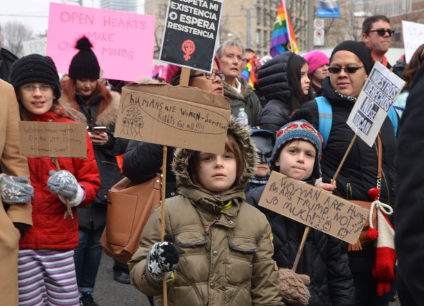 kids walking together in Womens March, toronto hold signs that they have made on cardboard. 