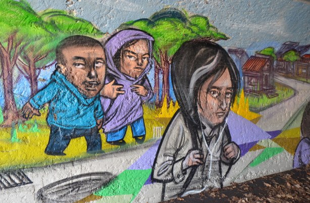 mural by elicser in the tunnel that is a railway underpass - young people walking, one with earbuds on and one making hand signs 