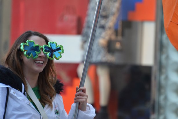 woman holding a metal flag pole, she's wearing big shamrock shaped glasses
