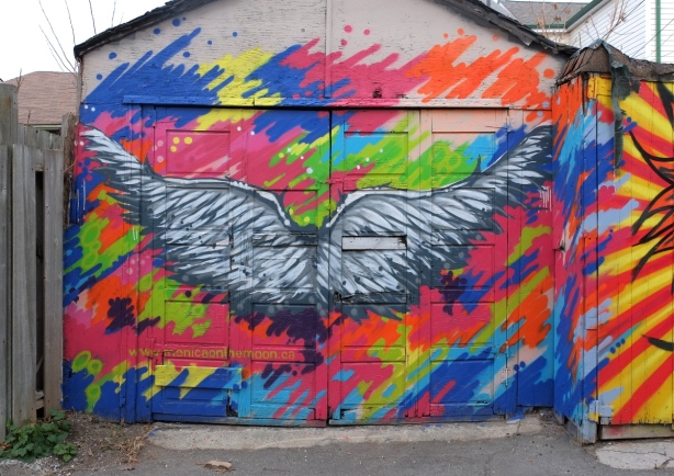 large black and white wings with multicolouredbackground - mural on a garage door in a lane