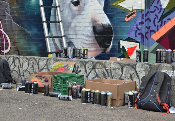 mural, white dog, with a row of spray paint cans in front 