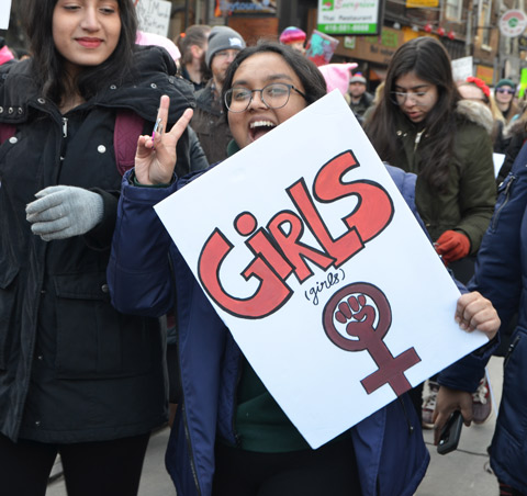 young woman giving peace sign and laughing, holding a girls sign 