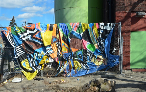fabric hanging from a rope beside a footpath, large green cylinder stoarge unit behind it. 