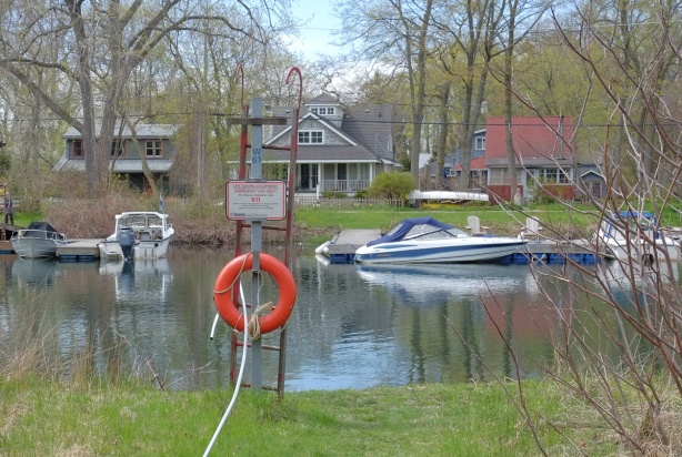 waterway, orange life ring and ladder on one side of the river, houses and docks, and boats on the other. r