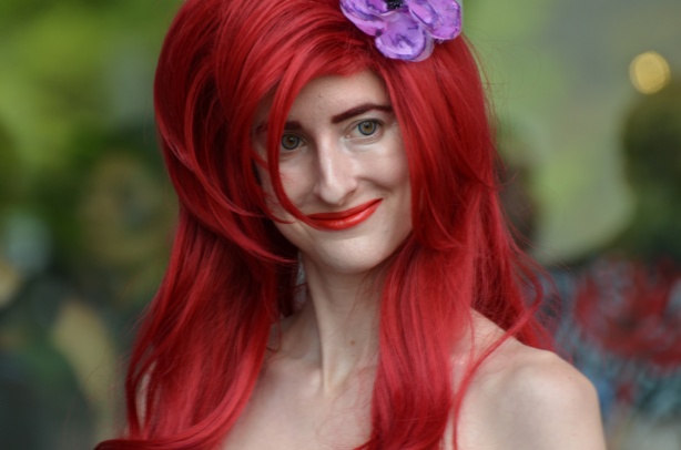 a woman dressed up as Ariel, the Disney mermaid, long red hair and a purple flower in her head 
