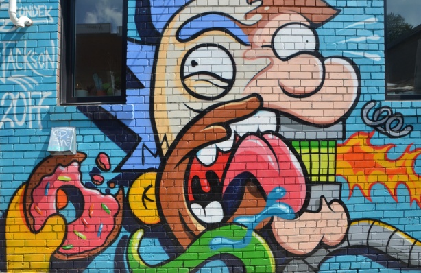 Simpsons parody mural by Jackson in a lane, man eating a donut and drinking Duffs beer. 