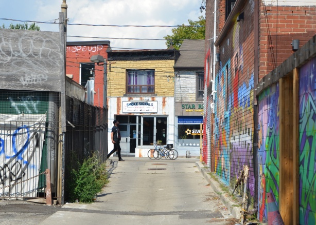 looking north up Skey Lane to Smoke Signals, a barbecue restaurant on Dundas West, a man is walking by on the sidewalk 