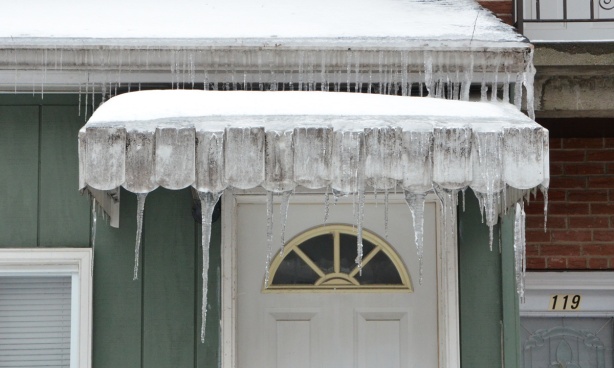 white door in green house, awning over the top of the door, icicles hanging from the awning and from the roof 