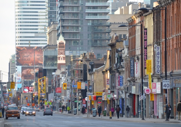 looking south on Yonge street on a sunny morning, sun is shining on the St. Charles tavern clock tower, tall buildings behind it 