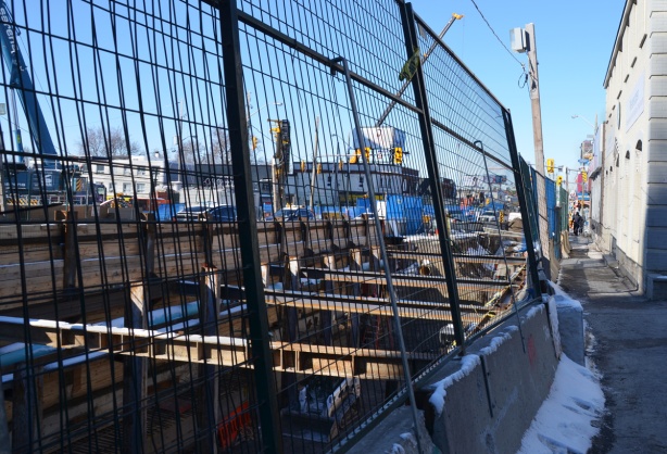 wire mesh fence in front of open pit excavation of underground LRT, steel cross beams and wood supports, 