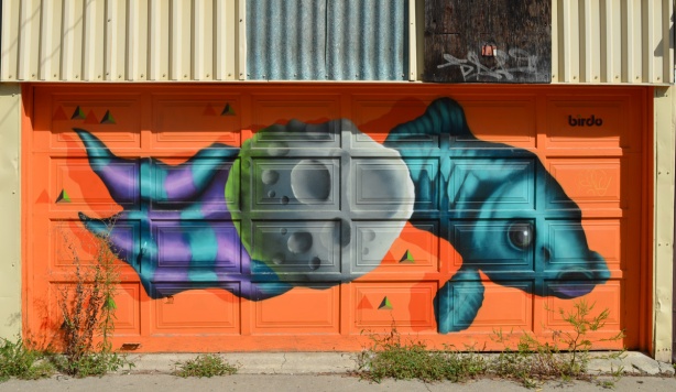 birdo mural on a garage door, orange background, fish swimming behind a stone, fish is teal and tail is purple and teal striped