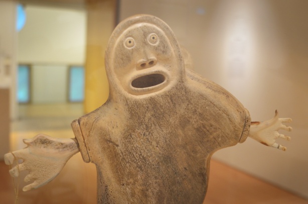 whale bone sculpture in art gallery, mother and child, large round face with open mouth and two outstretched arms with large hands 