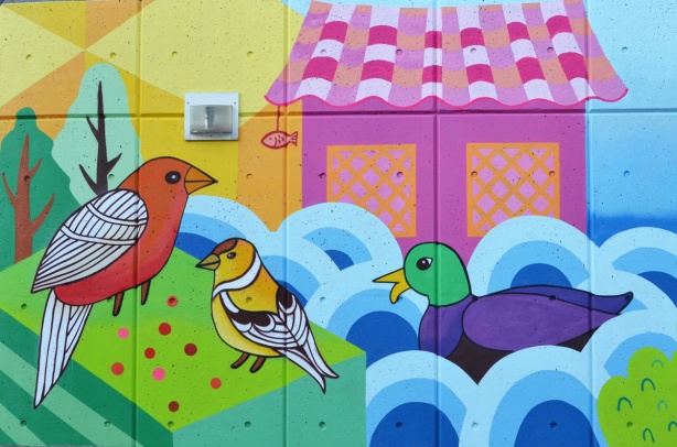 part of a mural by K J Bit Collective, mallard duck in water, goldfinch, and a cardinal in front of a pink building 