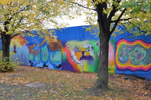 autumn trees in front of hoardings covered with murals, wallnoize, leaves on the ground, 