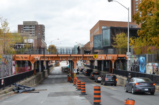 railway bridge over Bloor West near Dundas, painted orange, construction on one side of the road so traffic diverted to the other side 