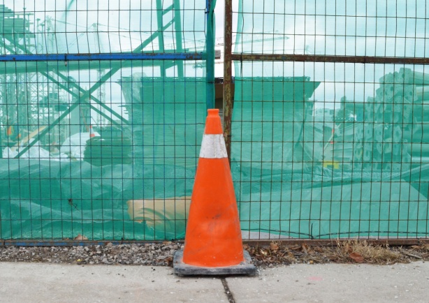 orange construction cone beside a fence with a green construction cloth covering over it 