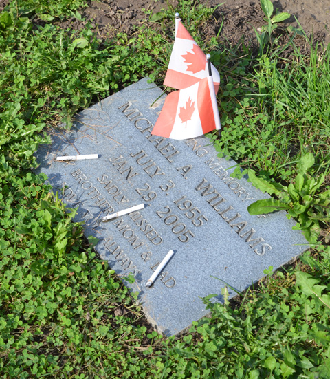 flat ground level memorial in a cemetery with three cigarettes and 2 small Canadian flags 