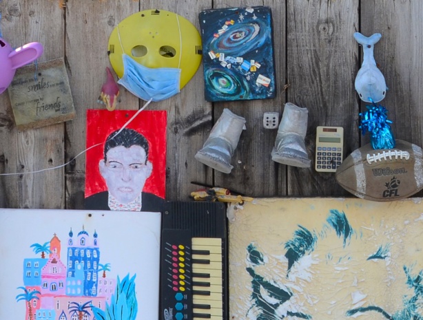 objects attached to a wood fence, a yellow plastic mask, small rubber boots, an old calculator, a small piano keyboard, a portrait of Marilyn Munro 